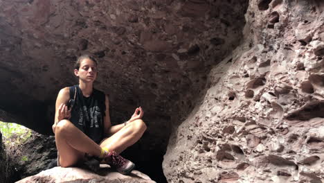 young woman wearing black shirt dries her face and starts meditating inside cave, all in slowmotion