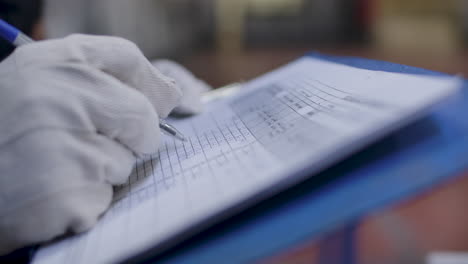 mano del trabajador en guantes escribiendo en la hoja de seguimiento en el lugar de trabajo