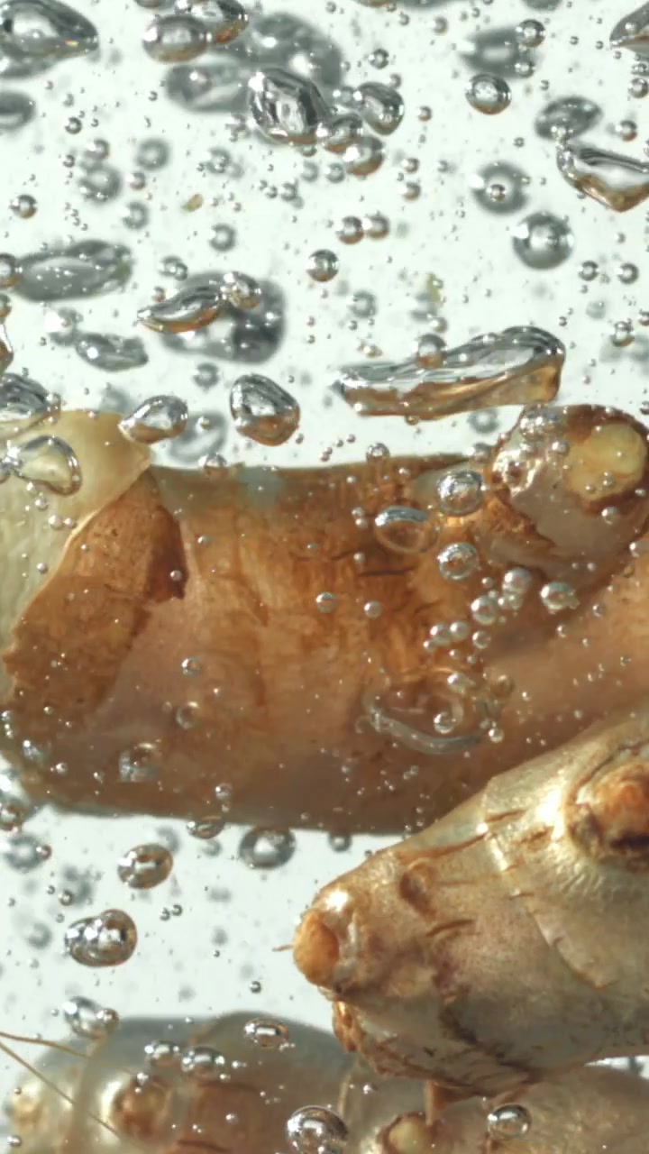 Radice di zenzero fresca che bolle in acqua limpida con bolle in risalita