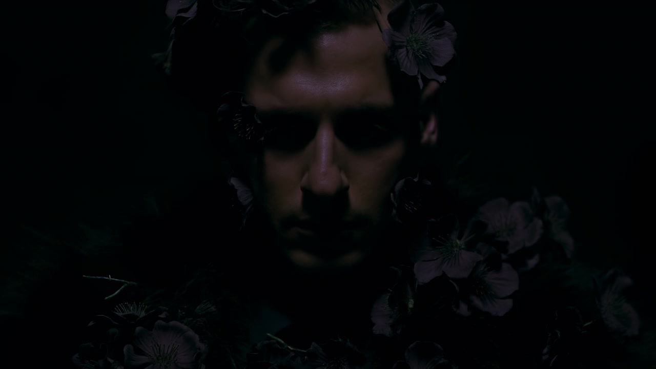 Volto maschile misterioso con fiori scuri che sfumano nell'ombra