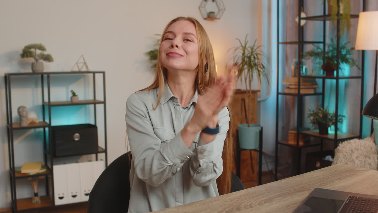 Happy woman claps hands and shows thumb up gesture congratulating on victory at home table desk