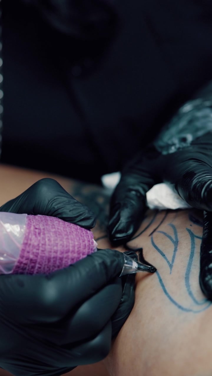 Tatuatore che usa la macchinetta per delineare il disegno sulla pelle