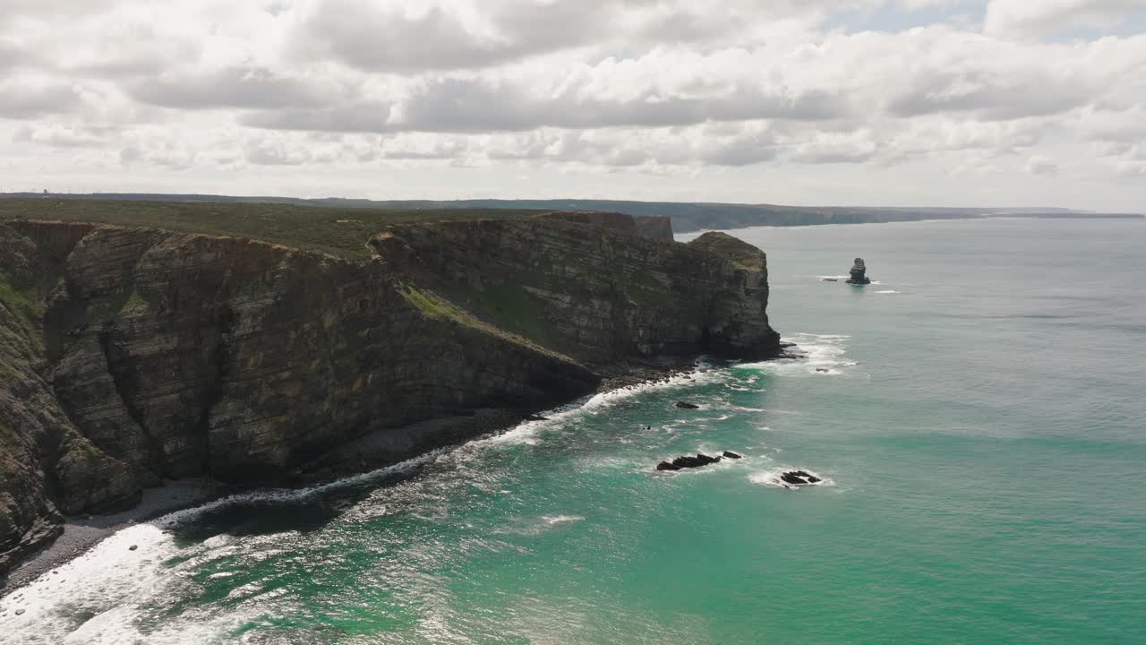 Aerial shot of rugged cliffs along a coastline with turquoise water on a sunny day