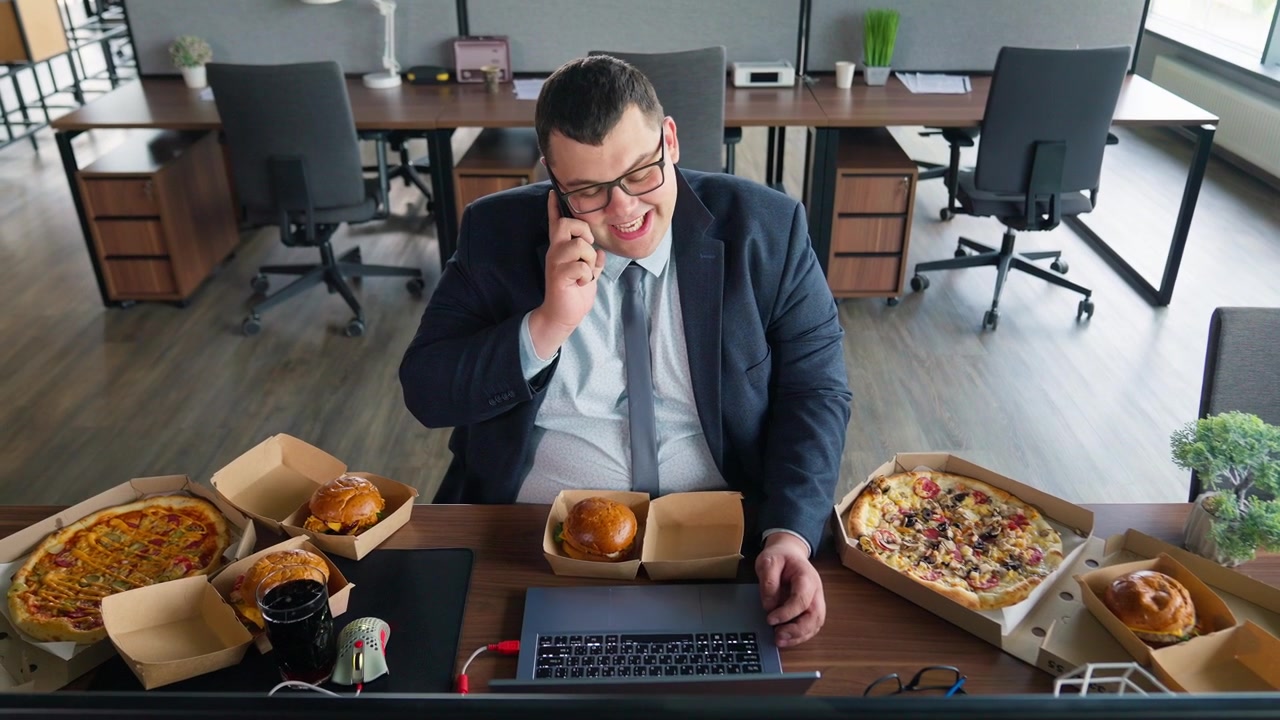 Uomo d'affari che lavora al portatile e parla al telefono, circondato da fast food