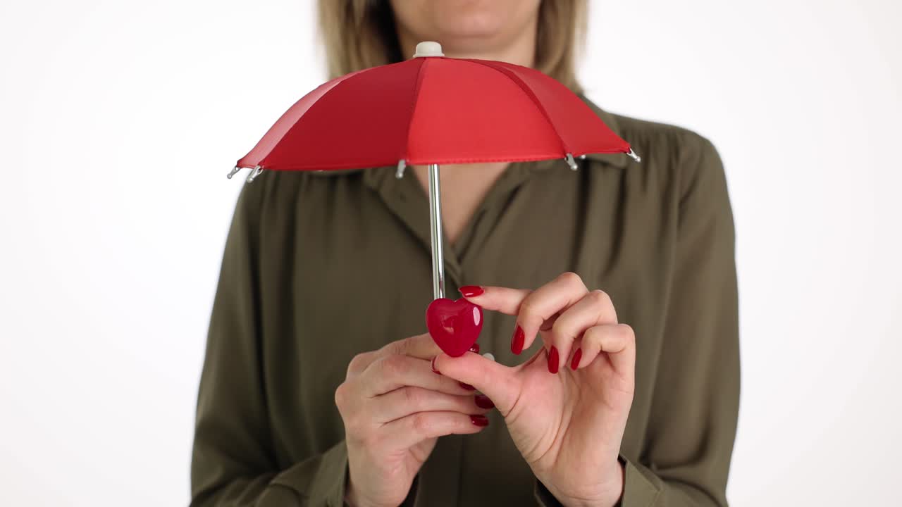Donna copre il cuore con un ombrello rosso contro un muro bianco.