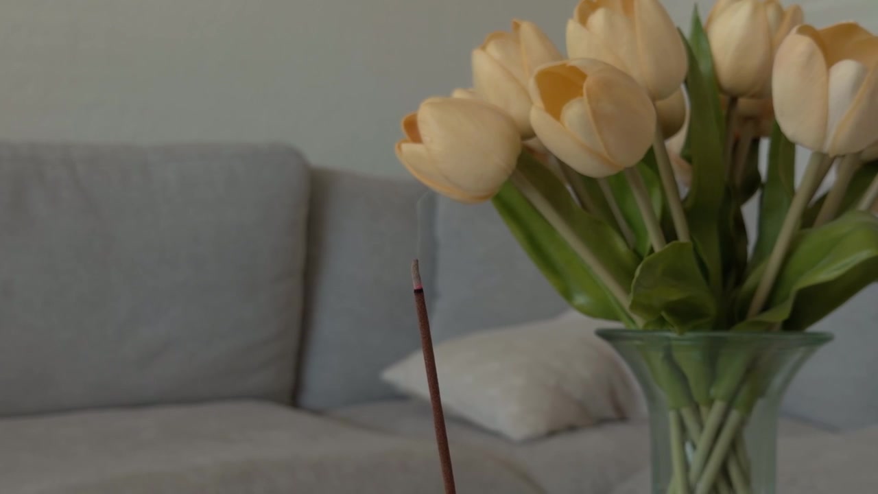 Gros plan fixe de fumée d'encens flottant à côté de fleurs et d'un canapé à l'intérieur