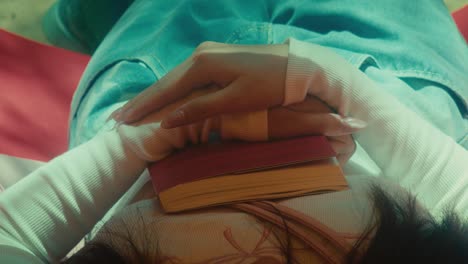 young woman relaxing rest and patiently wait someone while laid on a park holding a book on her chest