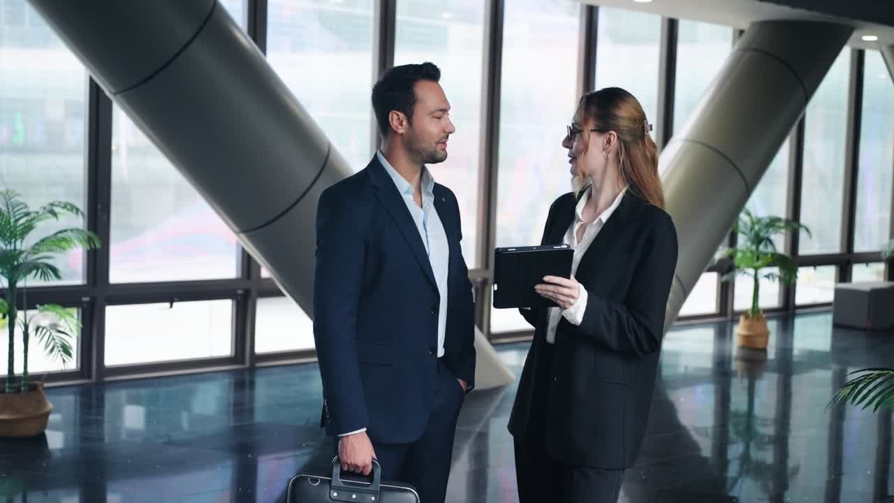 Businesswoman With A Tablet Discussing a Report With A Professional Businessman Holding a Brief Case In A Modern Office Atrium. - medium shot