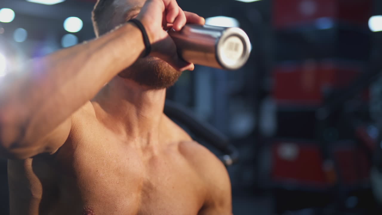 Sportsman drinking water. Sporty resting. Bearded guy having break after doing exercise on blur gym background. Handsome athletic man relax after training workout.