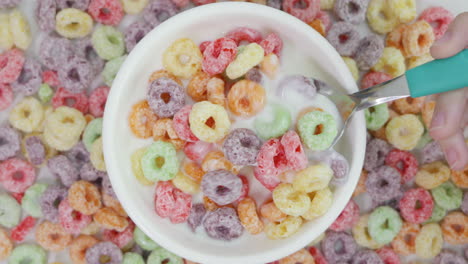 person spooning colorful corn ring cereals into a bowl of milk