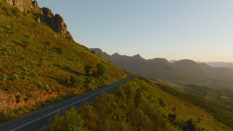 Forwards-fly-along-road-leading-through-mountain-landscape.--Scene-lit-by-bright-light-of-setting-sun.-South-Africa