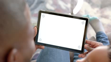 Happy-african-american-father-and-son-using-tablet-at-home-with-copy-space-on-screen,-in-slow-motion