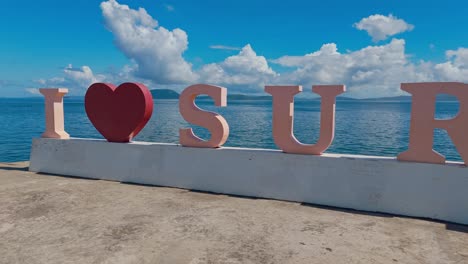 I-Love-Surigao-signage-by-the-bay-with-a-heart-shape-in-the-middle,-handheld-panning