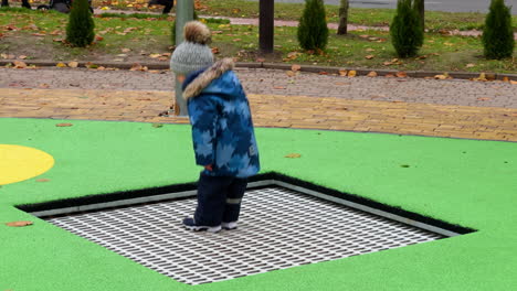 happy energetic toddler boy wearing warm clothes jumps on the trampoline outdoors. joyful baby on the playground in late autumn.