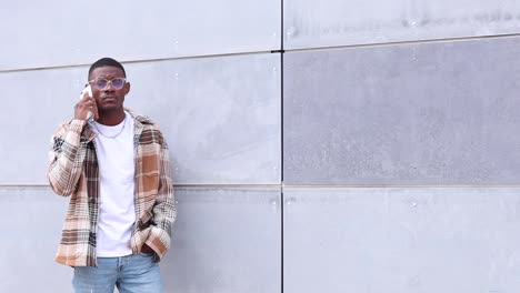 ethnic guy speaking on smartphone near wall