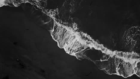 aerial from the top view of a beach with waves hitting up the sand, black and white shot of the beach