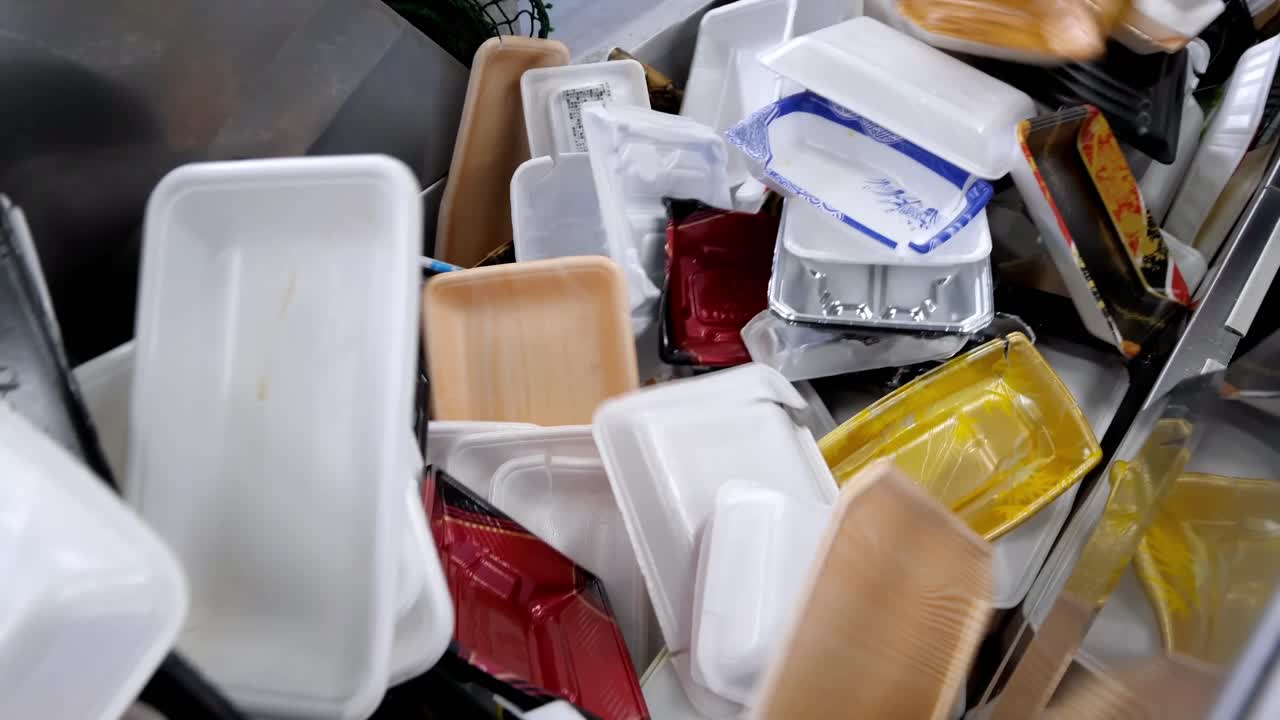 Plastic waste is being recycled. Various plastic items, including boxes, foam, and paper packaging, are being sorted on a conveyor belt at the recycling plant.
