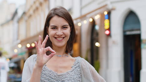 smiling woman giving the ok sign in a city street