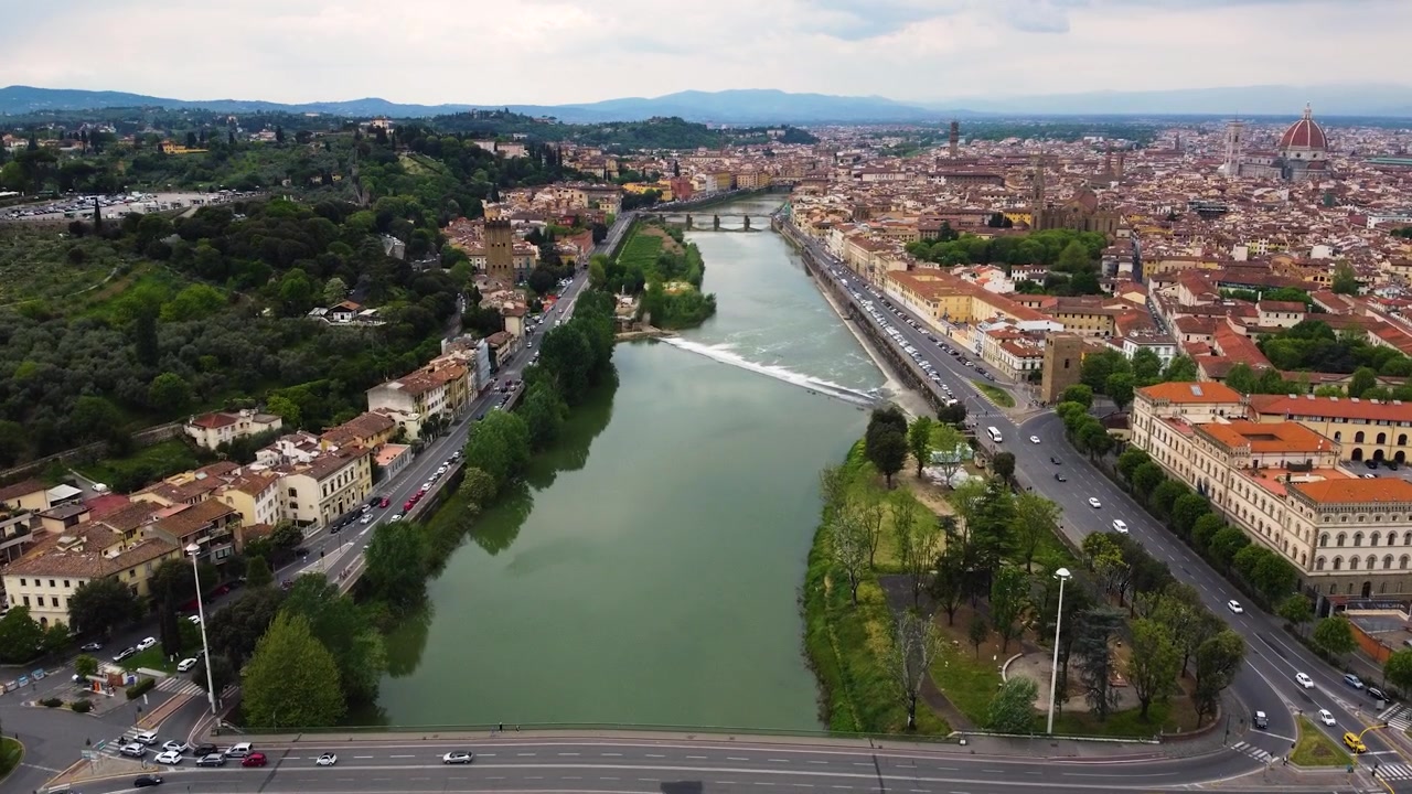 Ripresa con drone sopra gli argini del fiume Arno a Firenze, Italia. Centro storico con la cupola del Duomo e la Basilica di Santa Croce visibili tra i tetti, colline toscane sullo sfondo