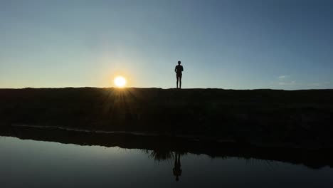 Skinny-young-man-exercising-jogging-in-place-at-sunrise-beside-a-lake