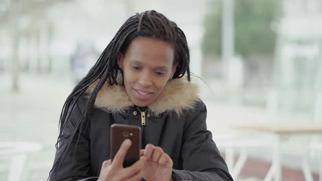 afro-american young girl with braids in grey jacket with fur hood sitting outside