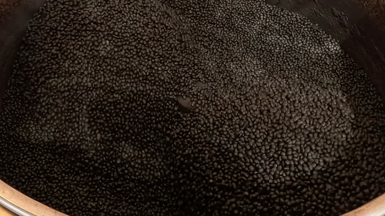 Uma imagem em close-up de ângulo alto de inúmeras castanhas rolando e assando dentro de uma panela grande