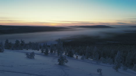 the-drone-follows-as-the-free-skier-climbs-up-the-slope-with-the-sun-setting-in-the-background