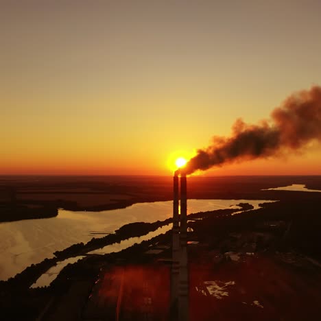 factory near the river in the evening. dark smoke goes from industrial pipes on nature background at sunset. air pollution in the environment.