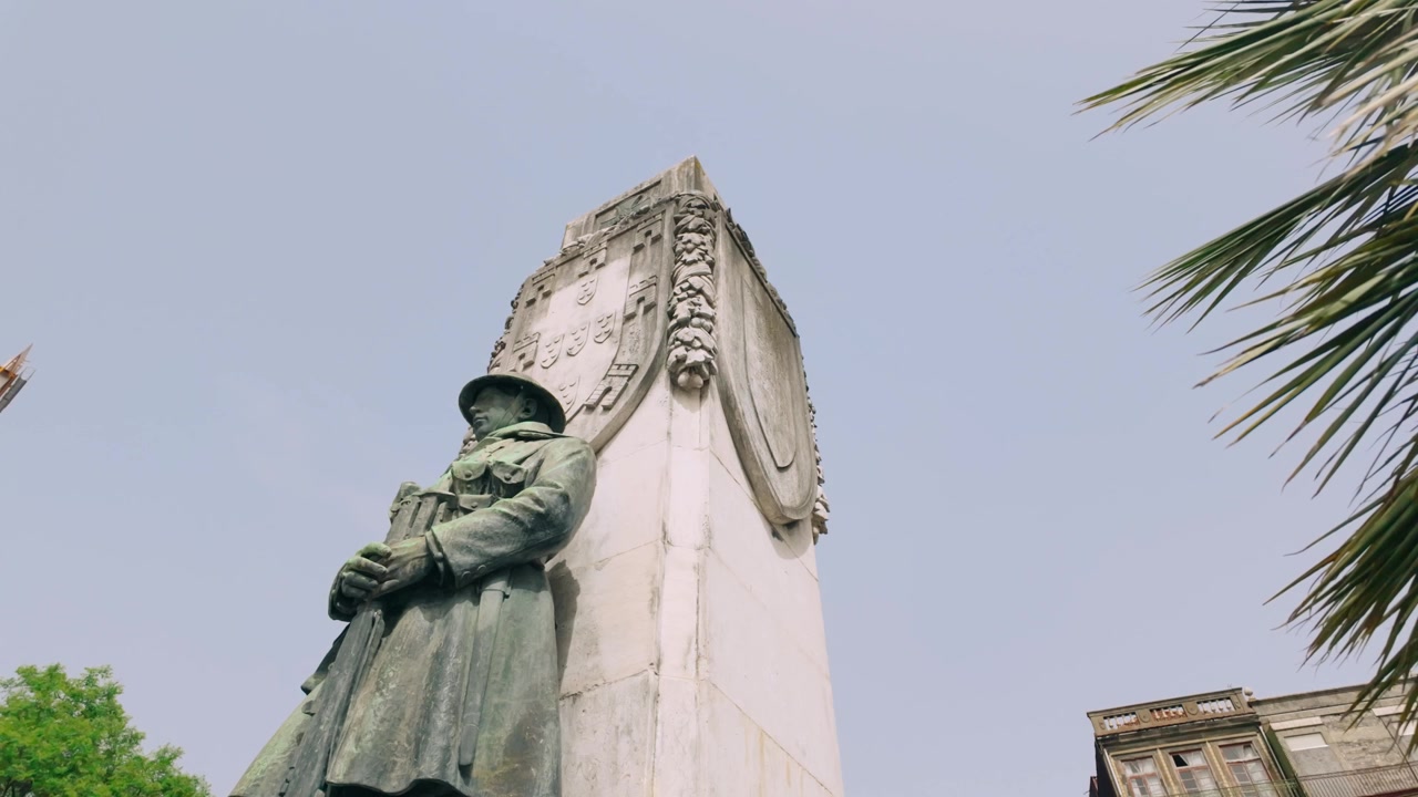 Suggestivo primo piano dal basso di un monumento storico a Porto, Portogallo, che si concentra sui dettagli intricati della statua del soldato e del suo imponente piedistallo, con fronde di palma che si protendono verso il cielo.