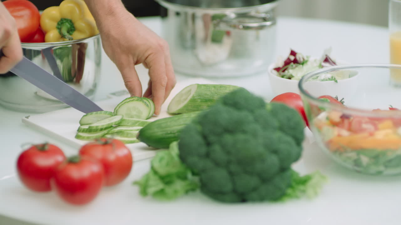 mano de hombre de primer plano cortando pepinos para ensalada fresca. chef hombre haciendo ensalada