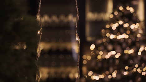 camera focuses on garlands of golden christmas lights in dark party room decorated with christmas tree