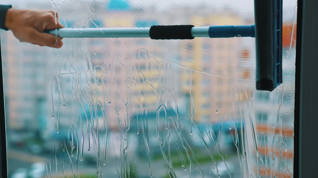 Window is cleaning with brush. Washing glass with clean water by special tool inside the flat. Professional window cleaning service. Close-up.