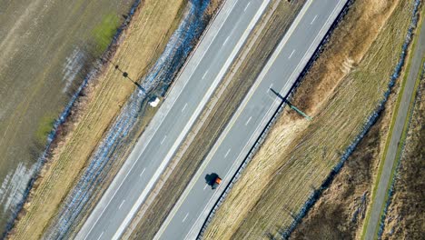 an overhead drone shot of a highway during the winter with dead grass and cars flowing both directions on the highway passing through the frame