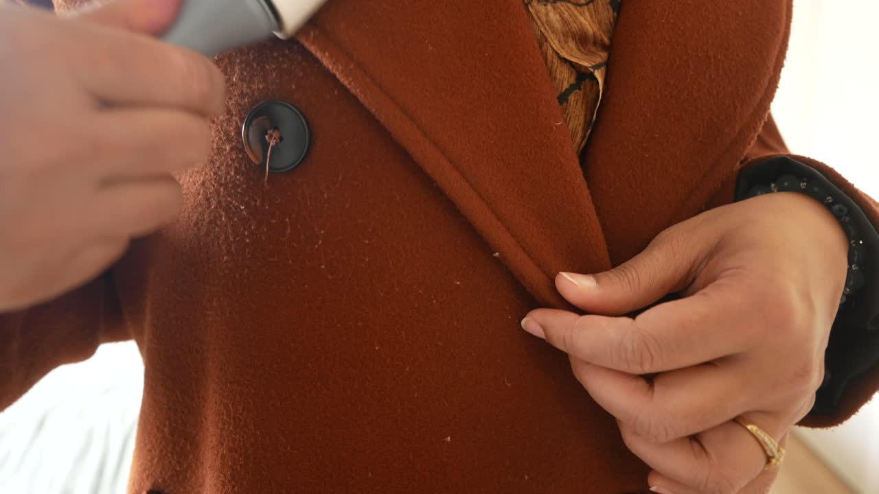 женщина чистит коричневое пальто с помощью ручного пылесоса