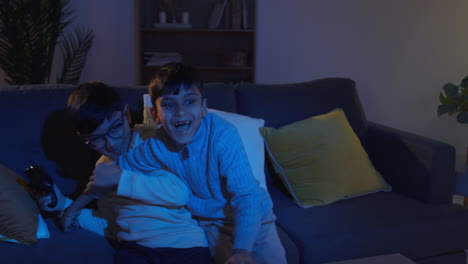 dos niños jóvenes en casa luchando por los controladores jugando en la consola de juegos de computadora en la televisión tarde en la noche