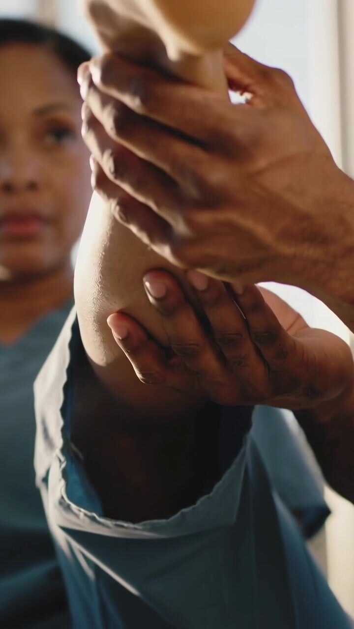 Vídeo vertical: Cuidador iniciando exame, segurando a perna do paciente na clínica, sentindo o calcanhar e a sola, calças azuis
