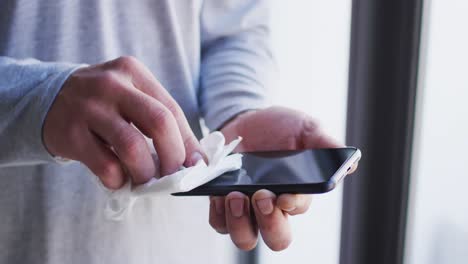 Mid-section-of-caucasian-man-cleaning-smartphone-with-tissue-in-slow-motion