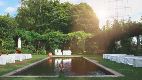 lonely scenic white marriage altar outdoors in the nature, white tablecloth cover, colorful green background and fountain pouring into a manmade pond or pool, beautiful reflection on the water surface