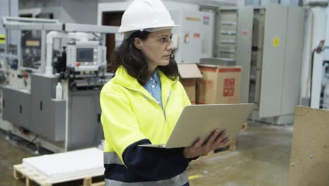 Serious-female-engineer-walking-with-laptop-at-factory