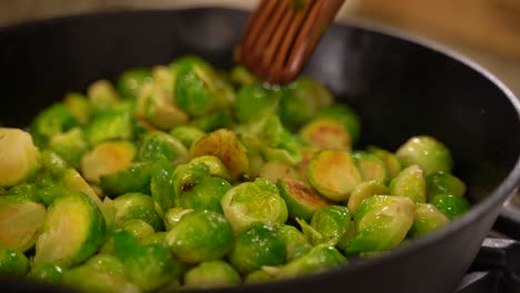 cooking roasted sautéed brussels sprouts in a cast iron pan skillet - stirring in parmesan with a wooden spatula - close up macro shot