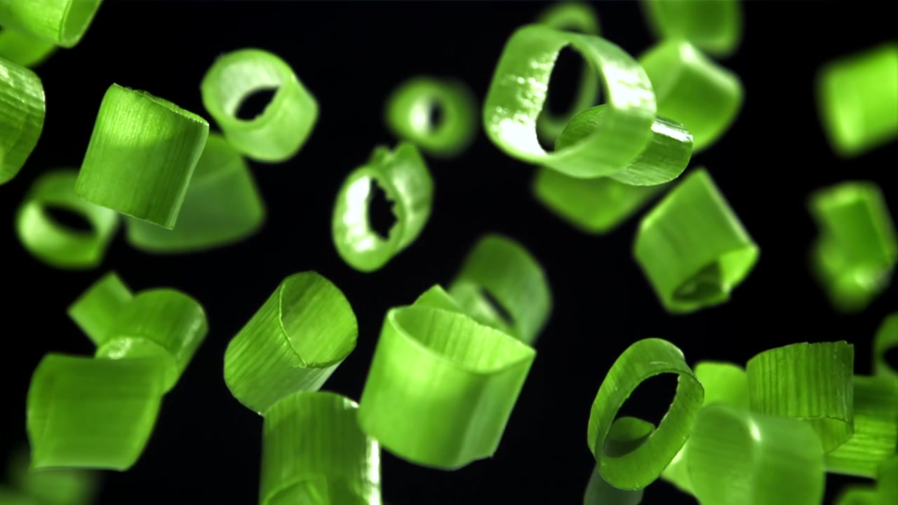 Chopped Green Onions Falling in Slow Motion Against Black Background