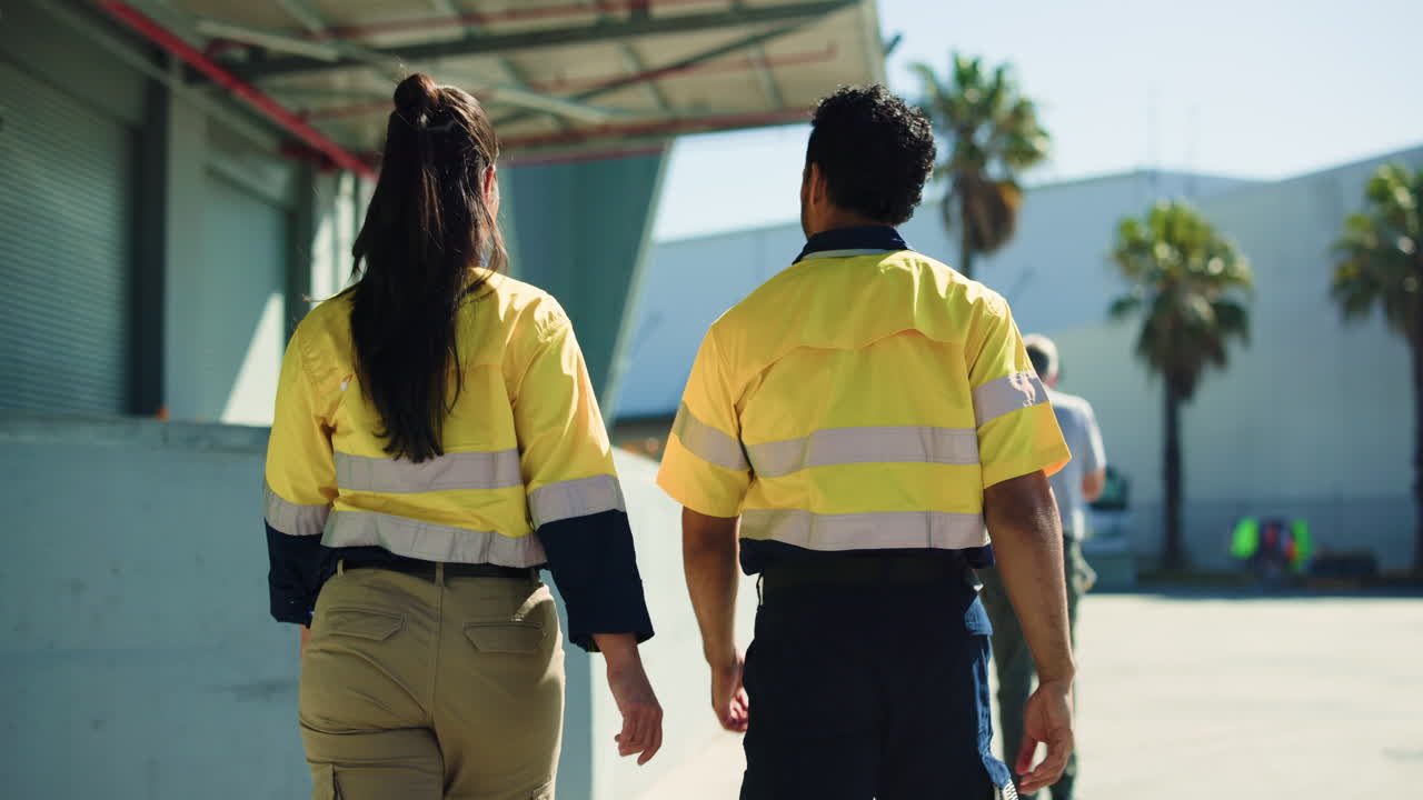 Dos trabajadores industriales con uniformes de alta visibilidad caminando y señalando en un almacén