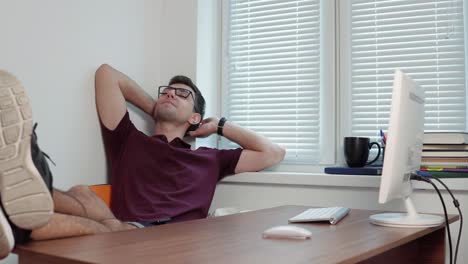 Young-office-worker-in-glasses-relaxing-in-office-with-his-legs-on-the-table-in-the-modern-office.-Break-during-the-working-time.-Shot-in-4k