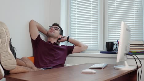 young office worker in glasses relaxing in office with his legs on the table in the modern office. break during the working time. shot in 4k