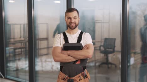 portret van een volwassen man in een werkuniform met gevouwen armen tegen de achtergrond van panoramische ramen in een modern kantoor