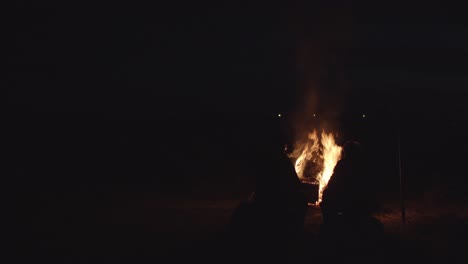 2 men silently sitting by big campfire at dark night