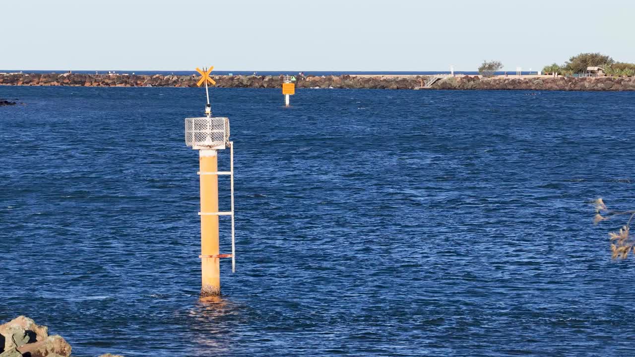 Aerial footage of a coastal waterway with a yellow marine marker under clear skies, showcasing natural surroundings