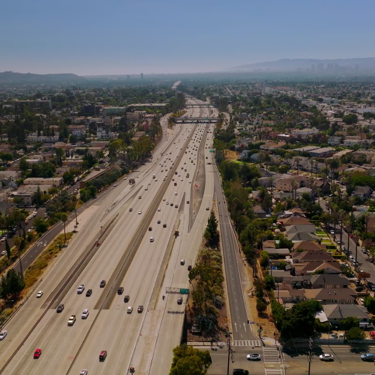 Multi-lane highway with numerous cars going through the big city. Sunny picture of Los Angeles from aerial view