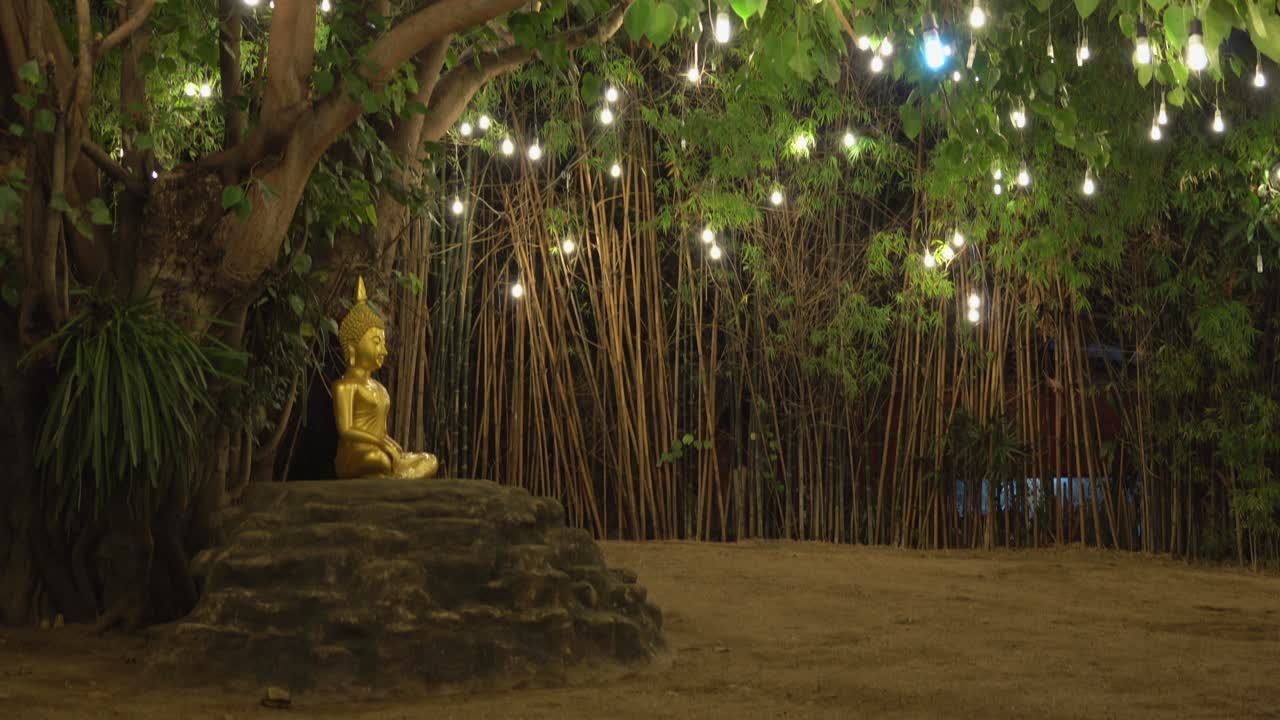 Buddha statue surrounded by lights in the middle of a man made little island surrounded by water.Lights reflection on the water and footage tilt up to the statue.