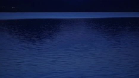 calm dark blue water reflecting moonlight at night with rippling surface and city lights in background creating a serene and peaceful atmosphere